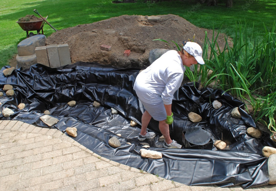 A homeowner installing the vinyl liner in the backyard pond