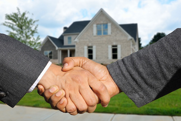 2 people shaking hands in front of a house