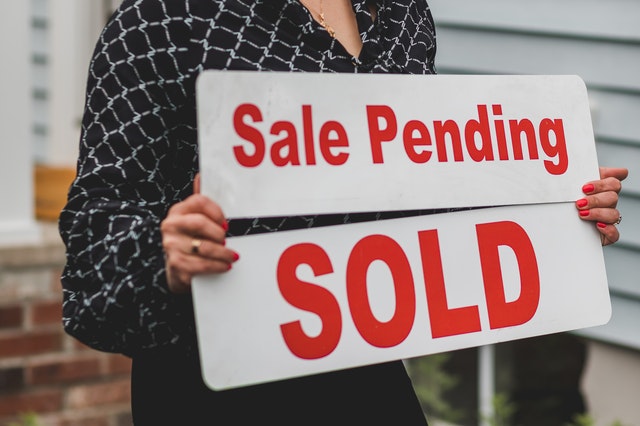 person holding a sale pending and a sold sign