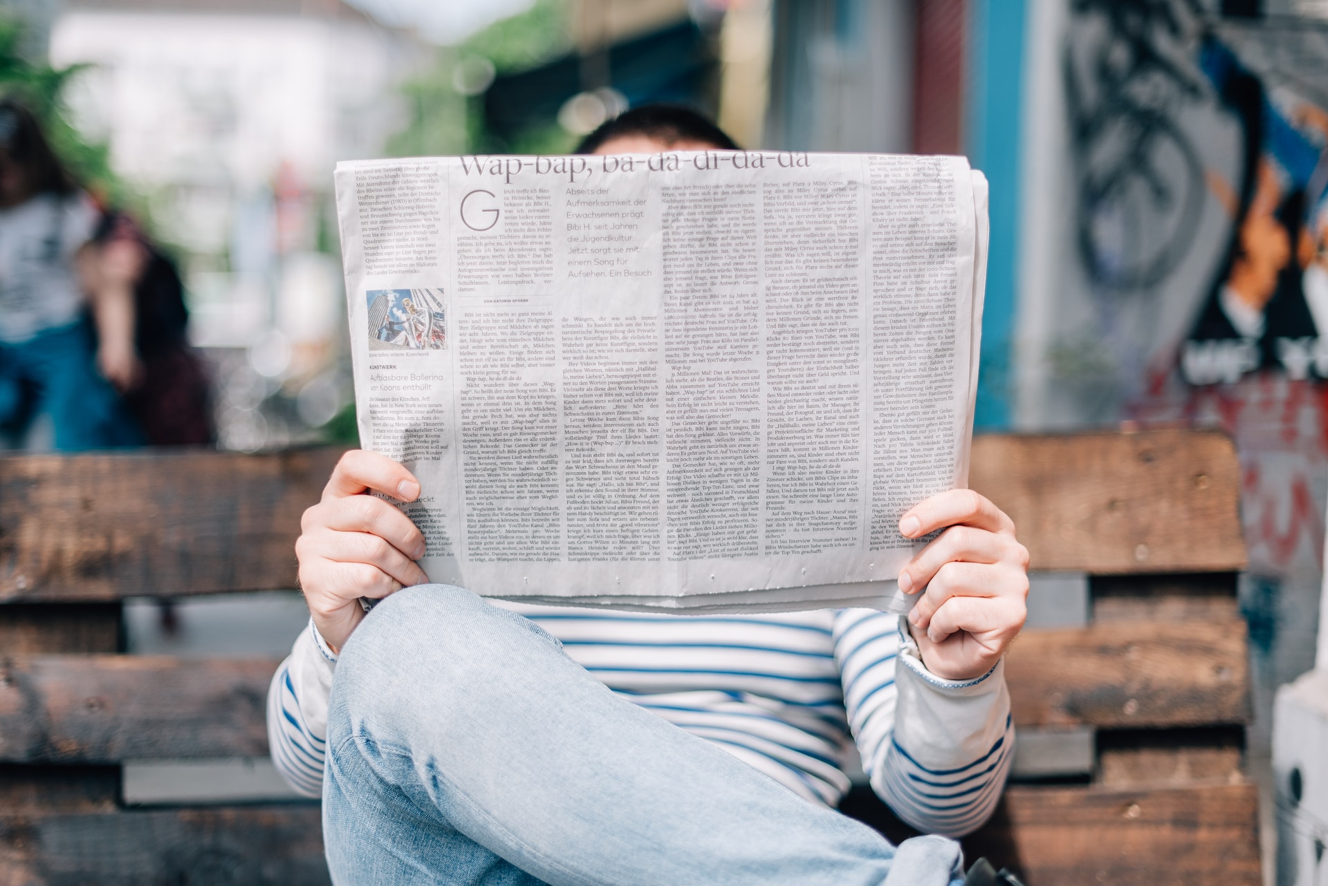 person reading a newspapar, sitting on a bench