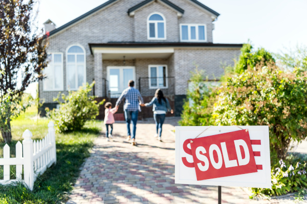 family holding hands walking towards a house. Sold sign