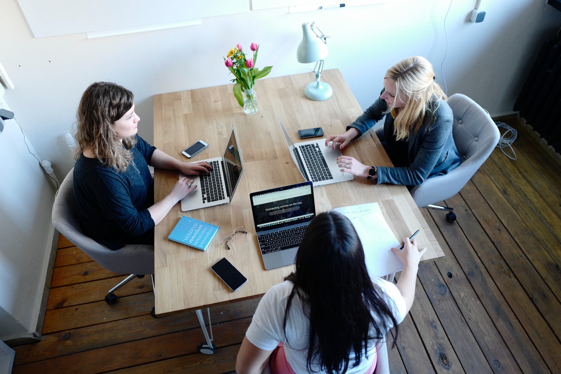 three people siting at a table wth laptops and cellphones