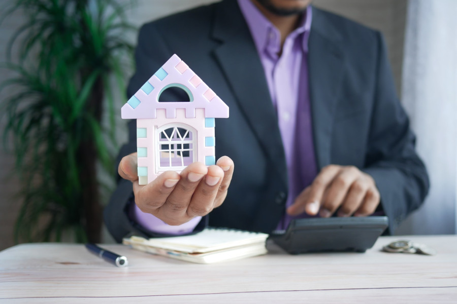 Person in a suit and purple shirt holding a house