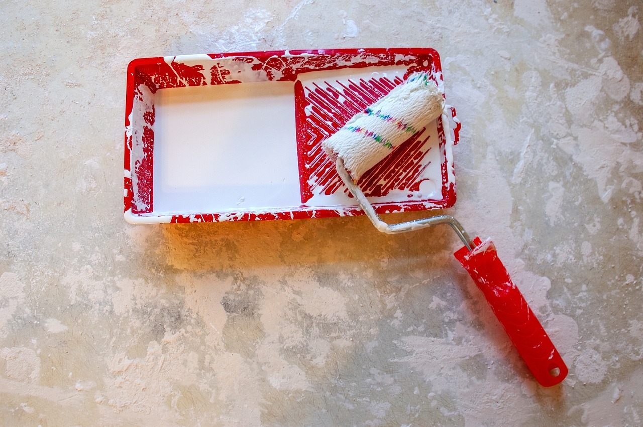 Red paint tray and a paint roller with a red handle. White paint. Image by Pixabay