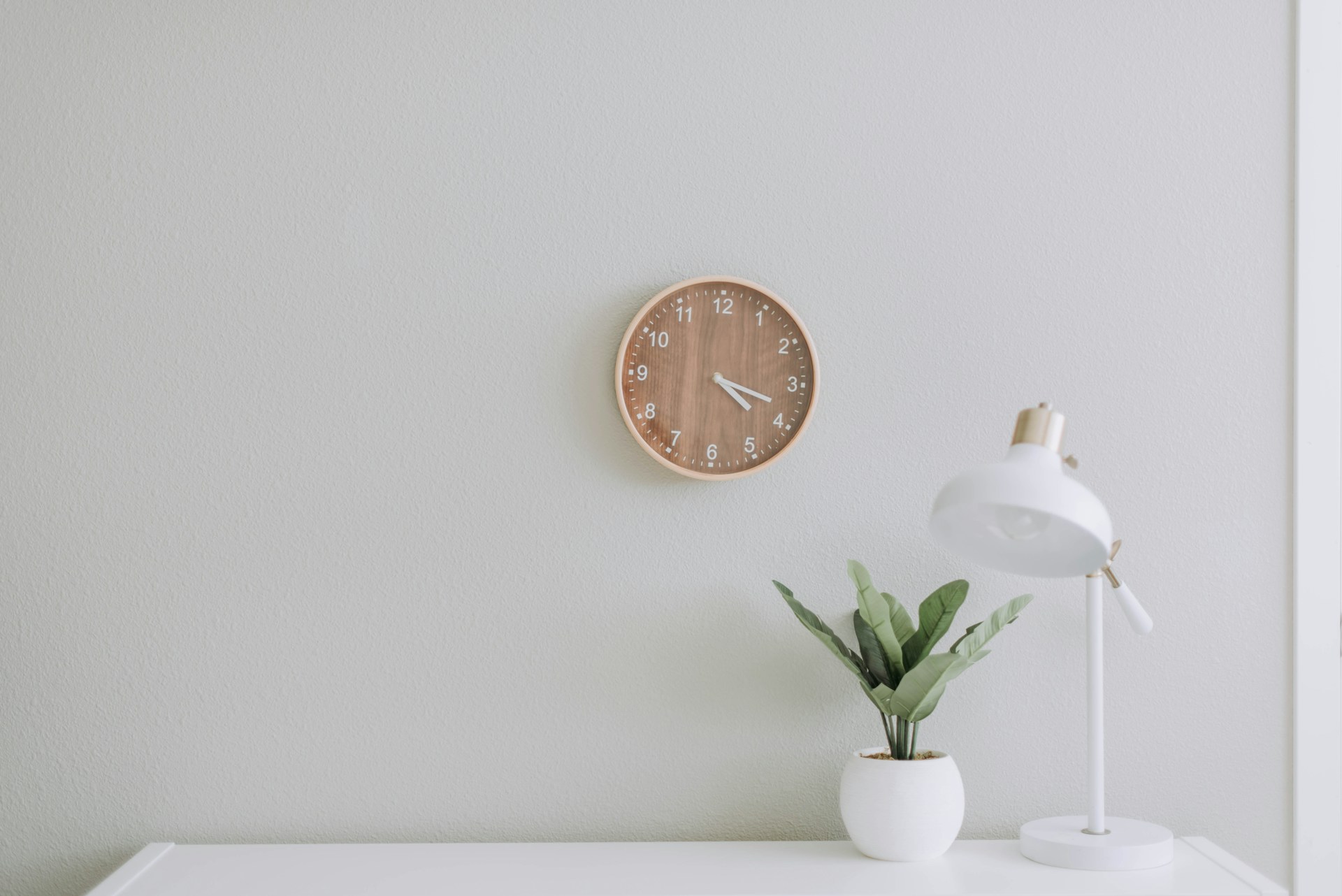 white desk, lant and lamp on desk, clock on wall