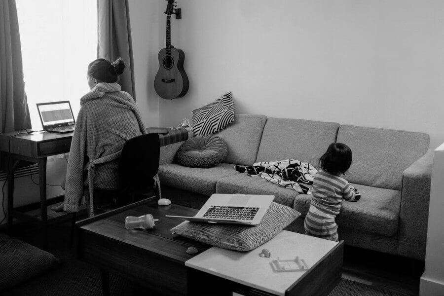 person working on a computer, child over by the sofa