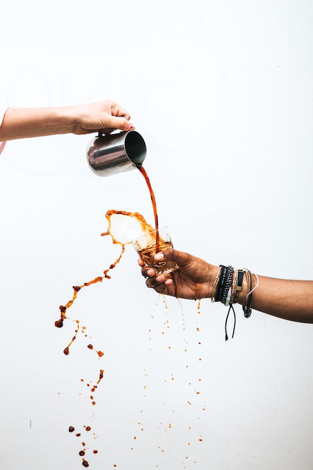 person pouring a drink into a glass, spilling