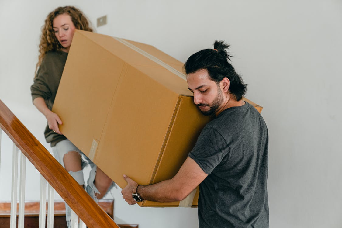 2 people carrying a box up the stairs