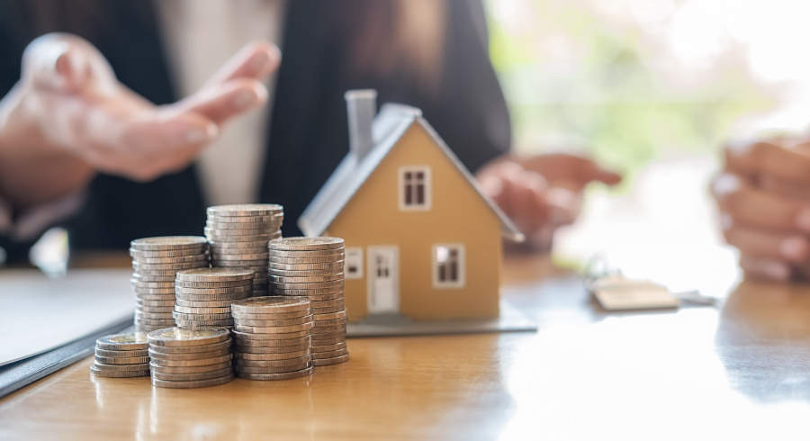 Coins, house on a table. Person in the background.