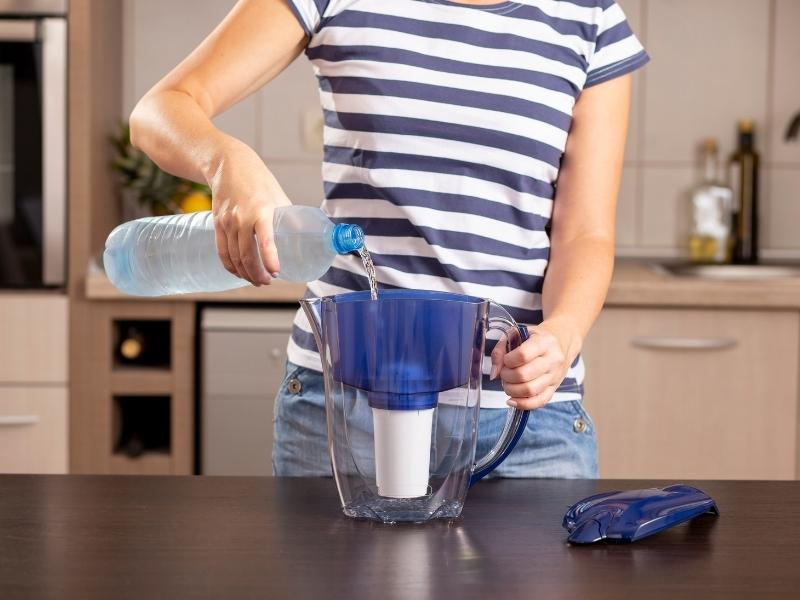 Person pouring a water bottle into a water pitchem with filter