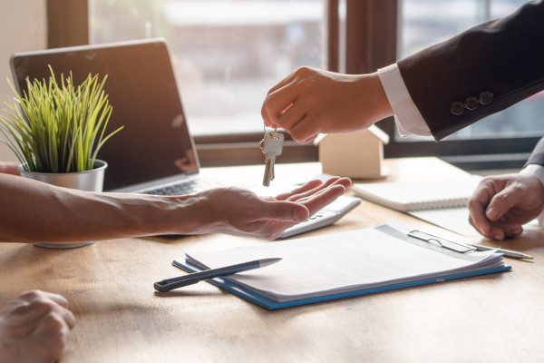 person handing over keys, paperwork on the table