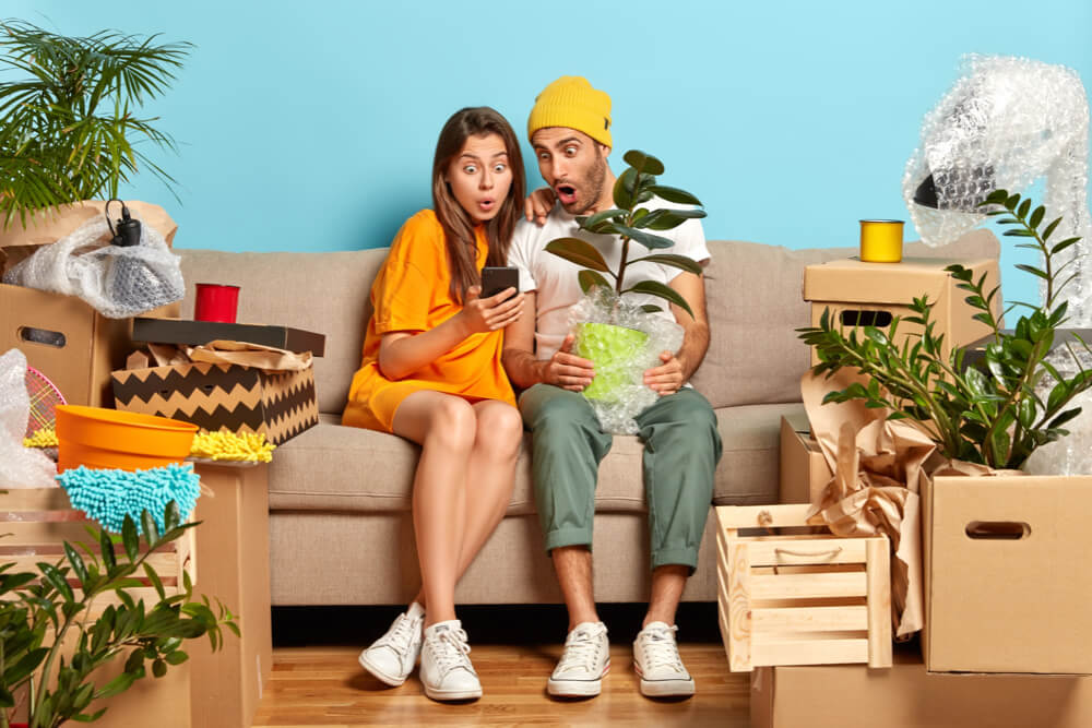 Two people on a sofa looking at a cellphone. Boxes all over the sofa and floor