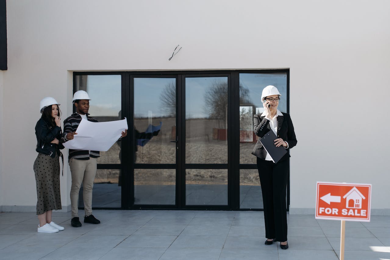 People standing outside a house for sale. White helmets on their heads. Image by Pexels