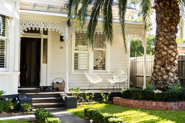 white house with a small porchs that has a couple of chairs on it. Large palmtree in the front yard.