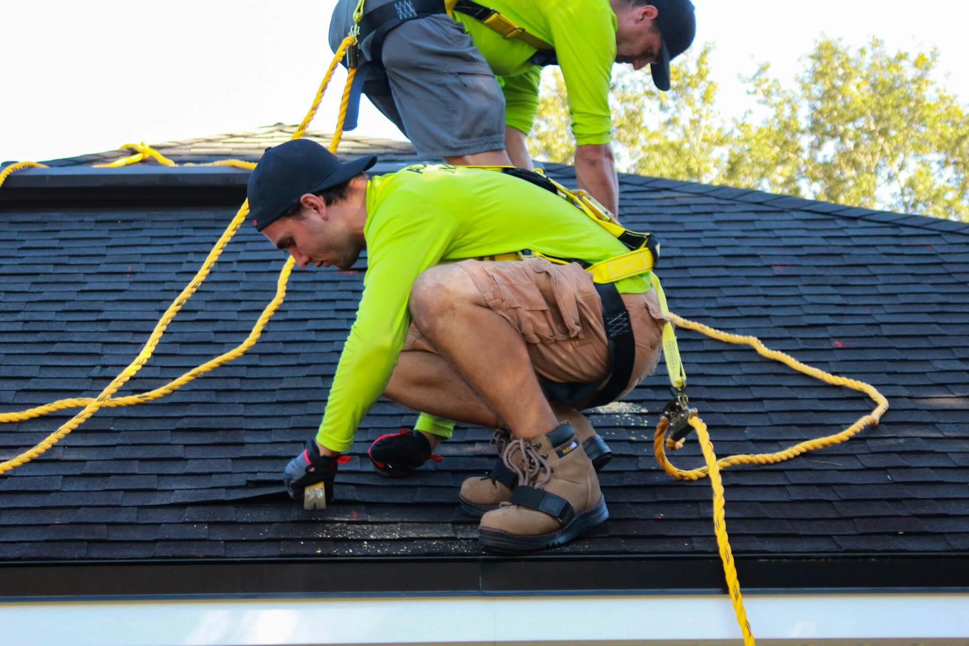 Two people working on a roof wearing yellow shirts. Image by Unsplash