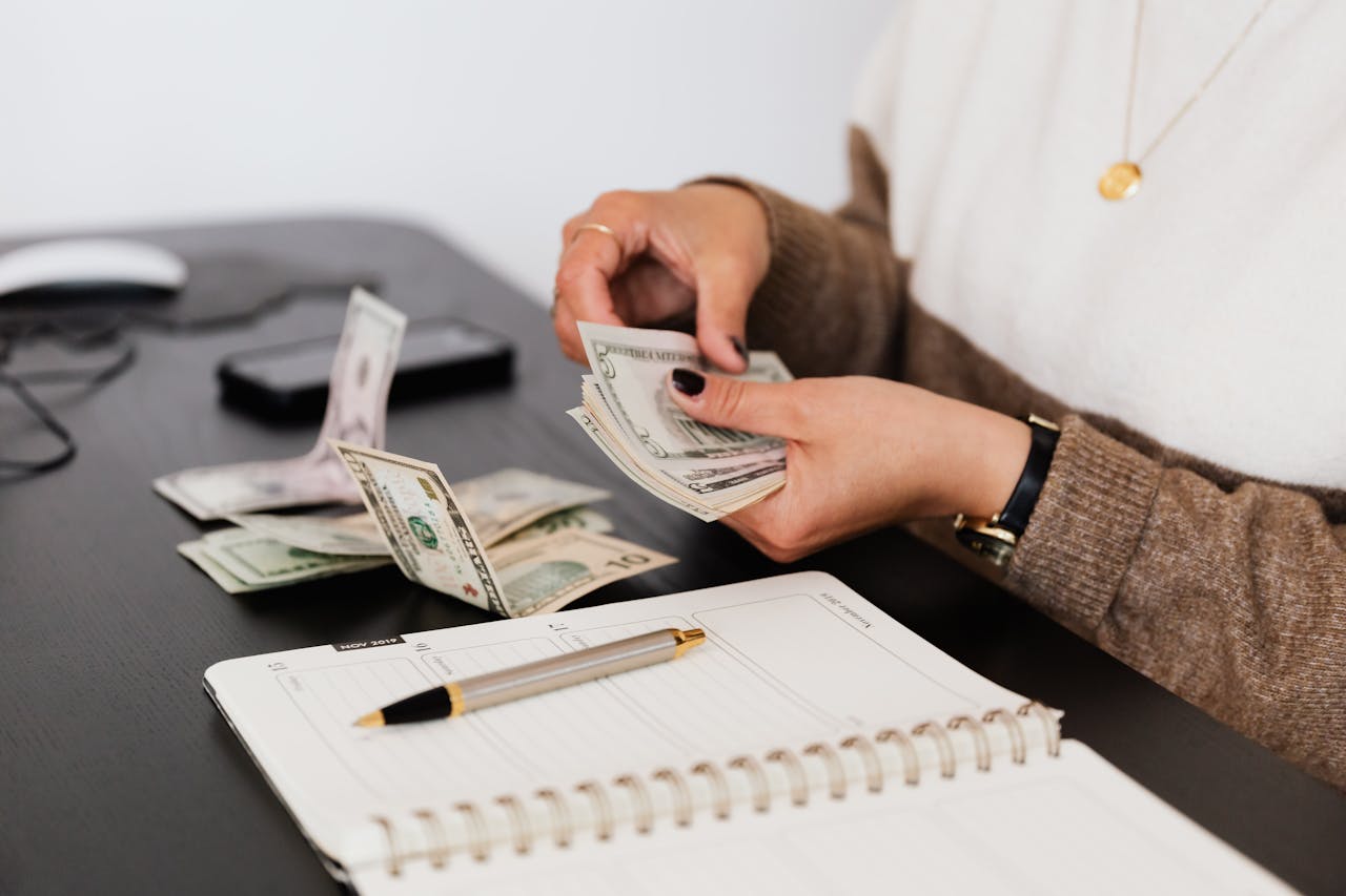 A person counting money in front of a desk. Image by Pexels