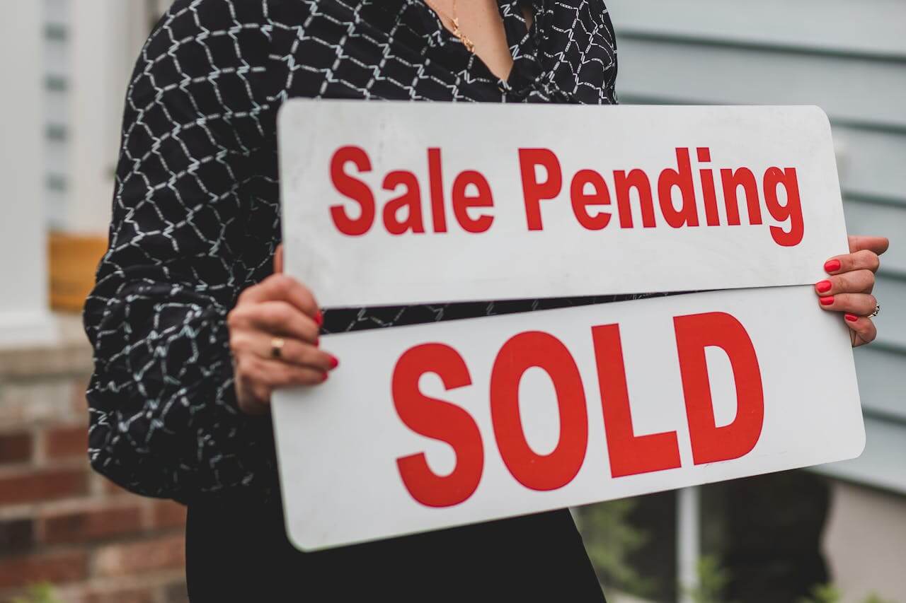 Person holding a for sale/sale pending sign. Image by Pexels