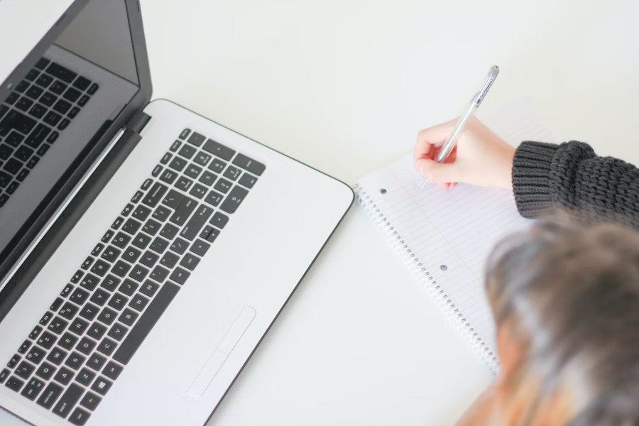 person writing on a paper, laptop