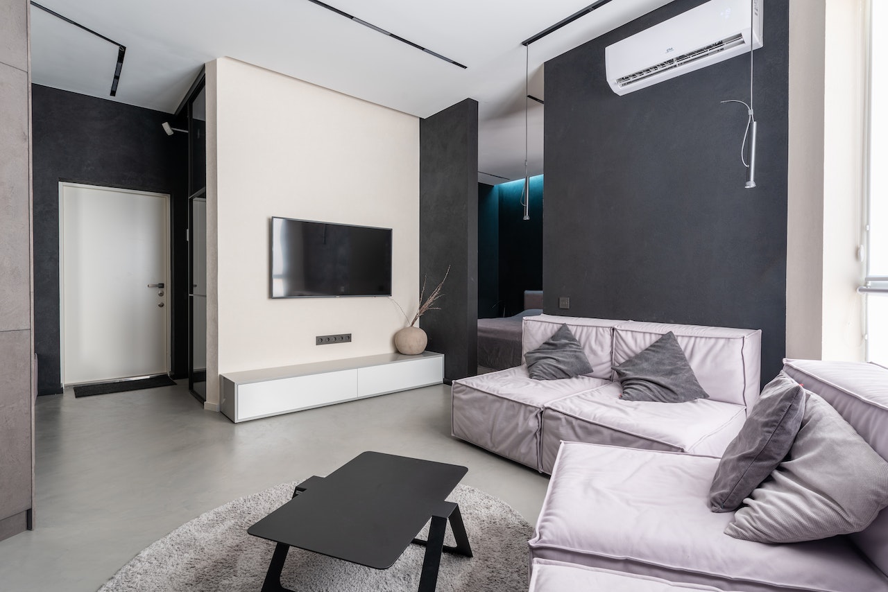 Livingroom, TV on wall, air conditioning unit on wall, grey and white walls, sofas and table