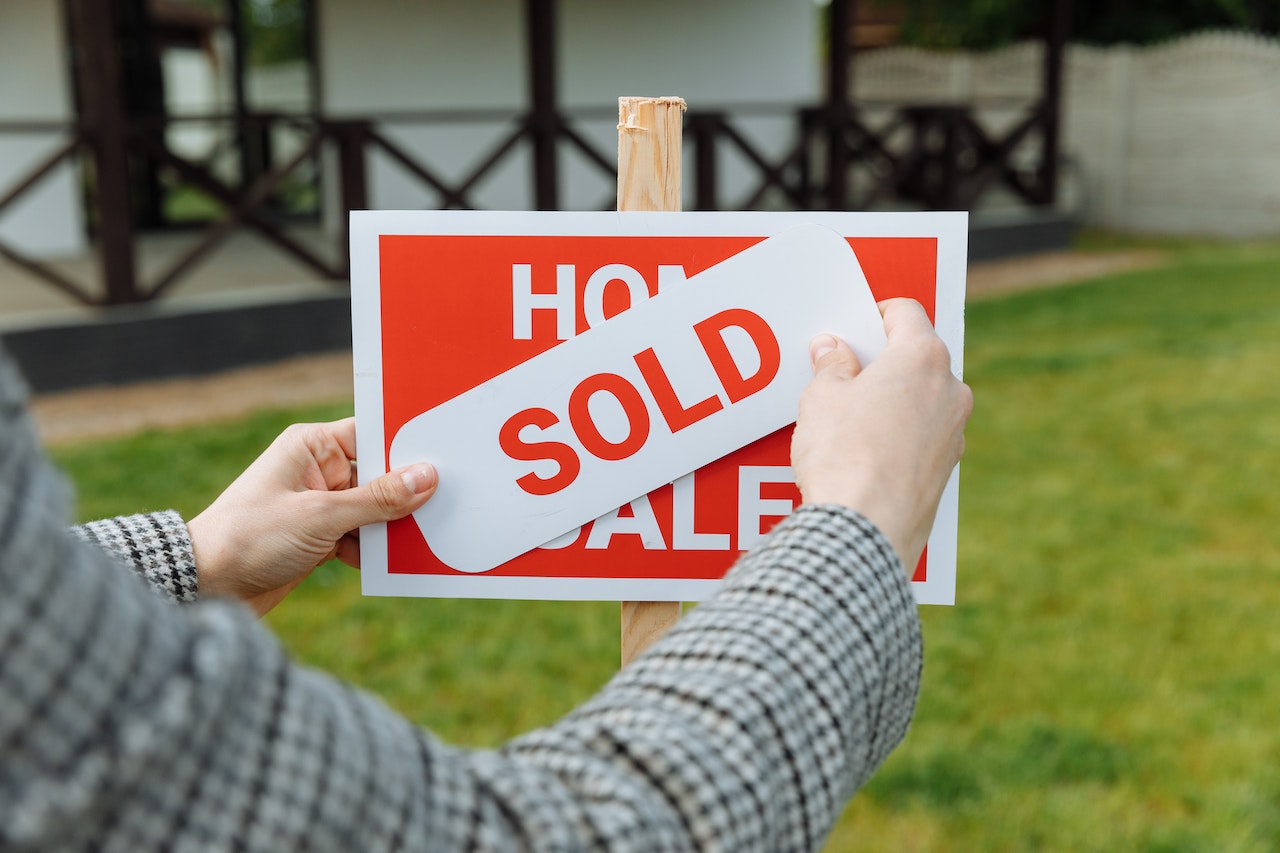 person putting a sold sticker on a for sale sign. Image by Pexels