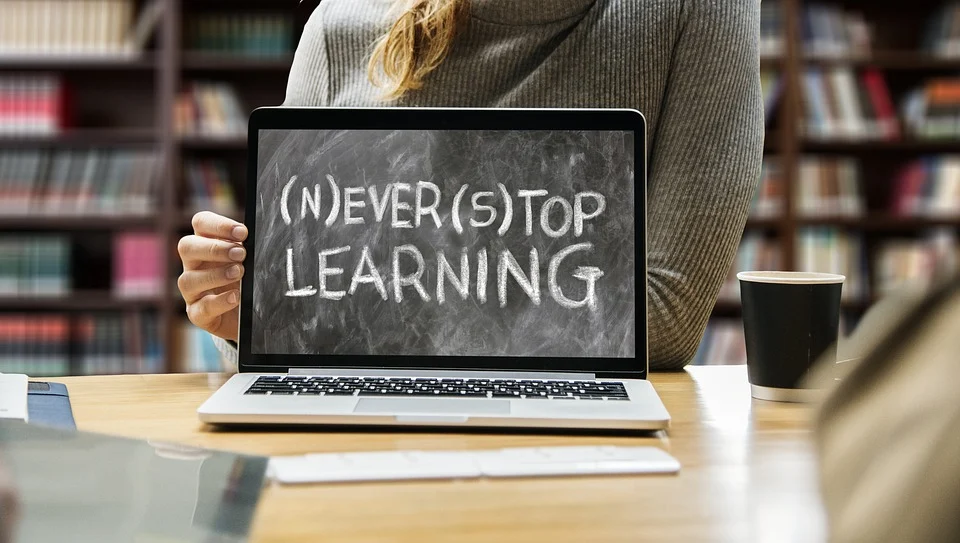 Person holding a laptop with the text (N)EVER (S)TOP LEARNING