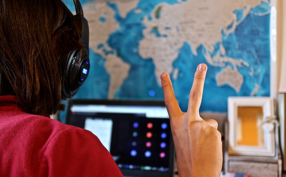 Person withheadphones in front of a laptop doing a peach sign