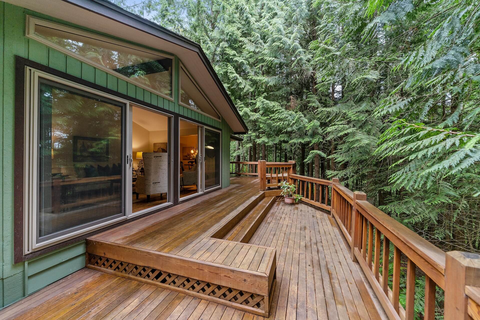 Large wooden deck on a green house with lots of windows