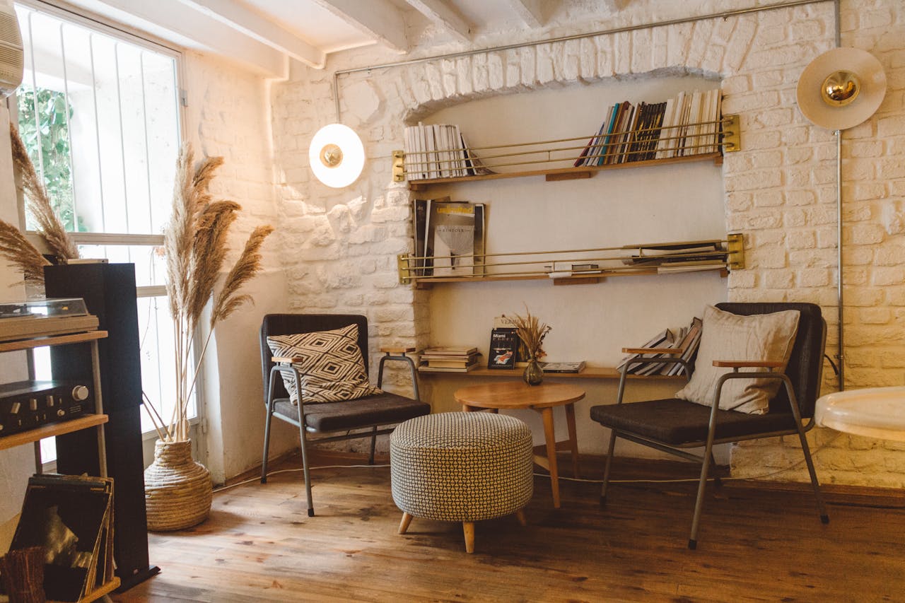 Cozy livingarea with w charis, a table and an ottoman. Magazines and books on a bookshelf. Image by Pexels